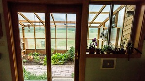 Visão através de uma porta de madeira com janela, revelando um jardim com plantas em vasos e um caminho de tijolos.