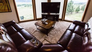 Uma sala de estar com uma televisão de tela plana grande, sofás de couro, uma mesa de centro e uma lareira.