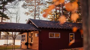 A cabin with a covered porch, a grill, and a view of a lake.