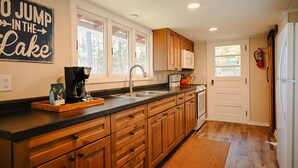 A kitchen with wooden cabinets, a black countertop, a coffee maker, and a sign that reads "GO JUMP IN THE LAKE".