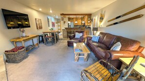 A cozy living room with a brown leather sofa, wooden coffee table, and a TV mounted on the wall.
