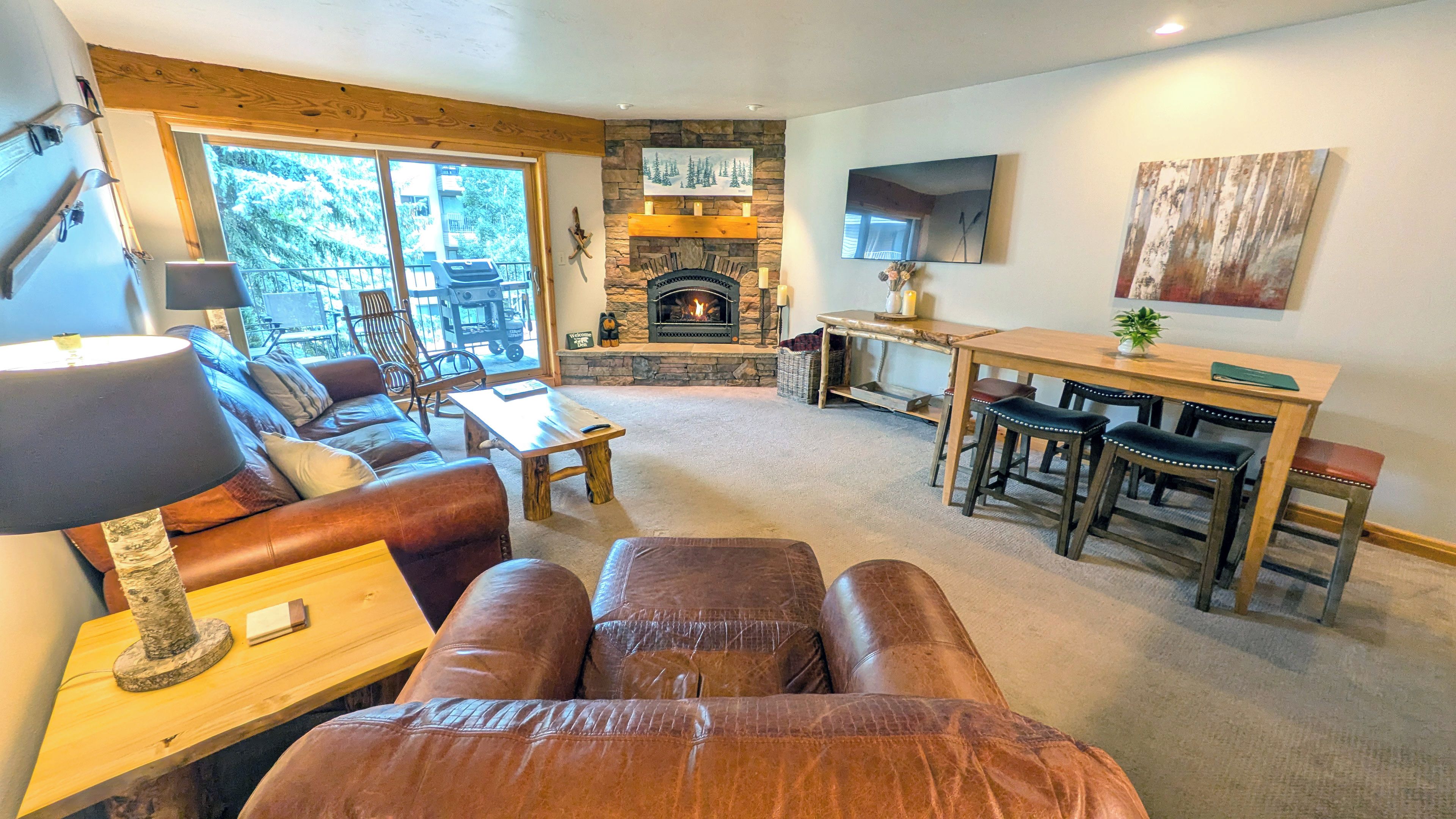 A cozy living room with a fireplace, leather sofa, and a dining area with wooden chairs.