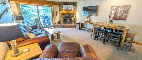 A cozy living room with a fireplace, leather sofa, and a dining area with wooden chairs.