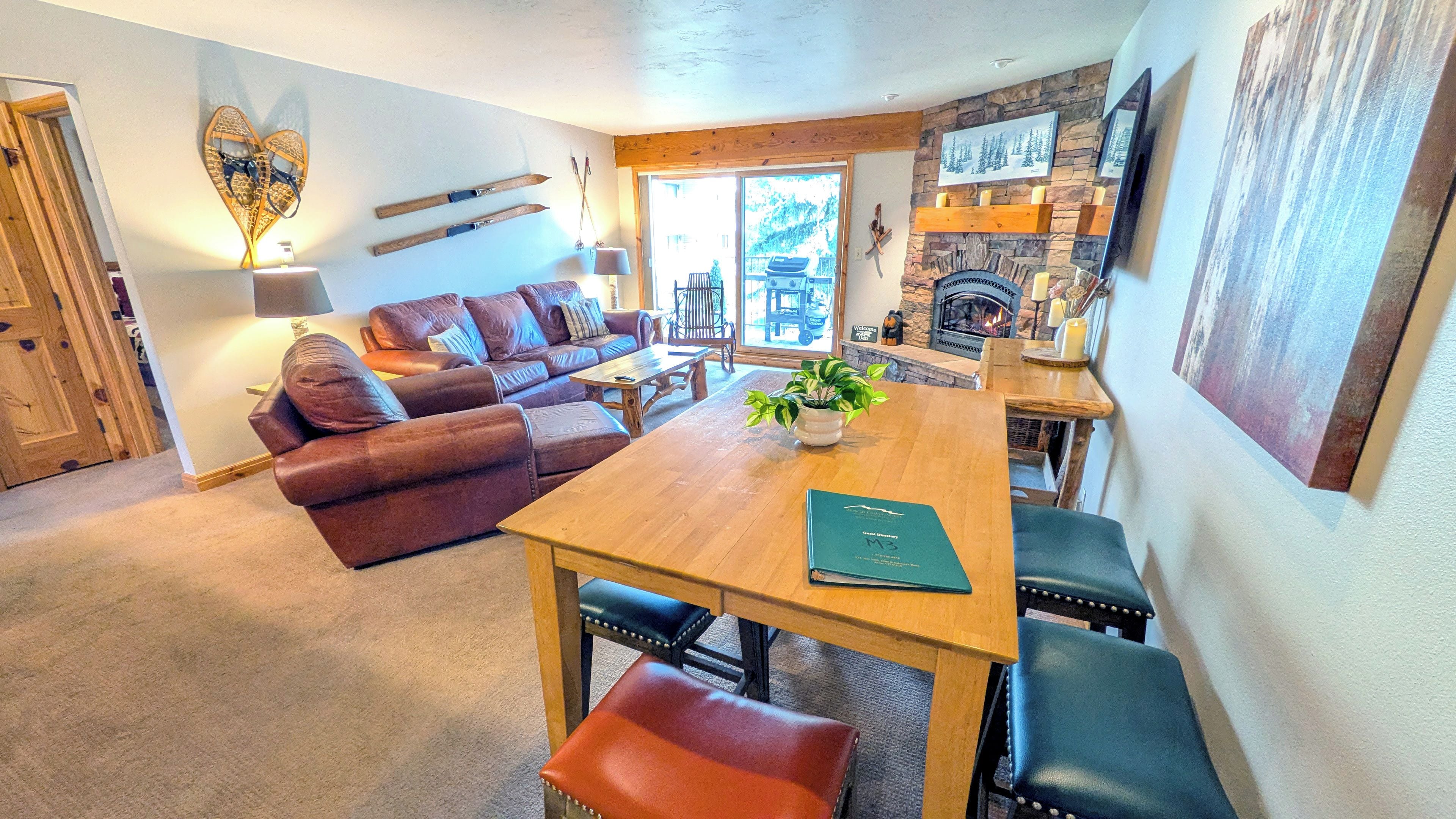 A cozy living room with a fireplace, leather sofa, and a dining area with a wooden table and benches.