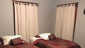Ein Zimmer mit zwei Betten, jeweils mit einem gemusterten Überwurf, einem Sessel und einem Schreibtisch mit Drucker.