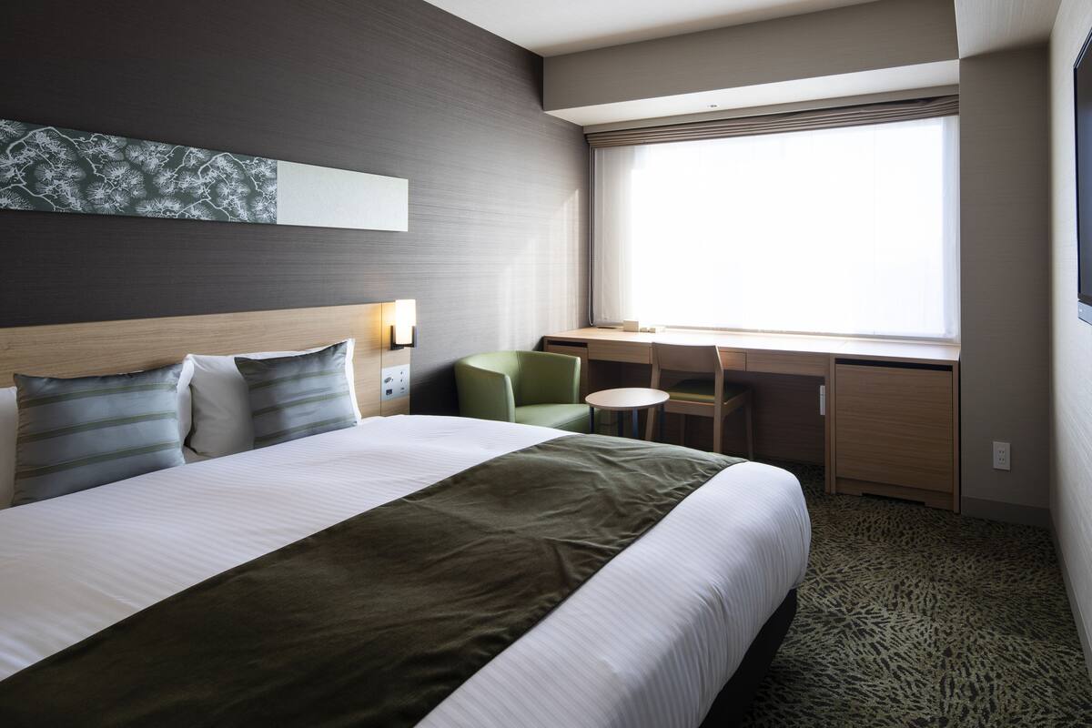 Une chambre d’hôtel avec un grand lit, un bureau, une chaise et une fenêtre.