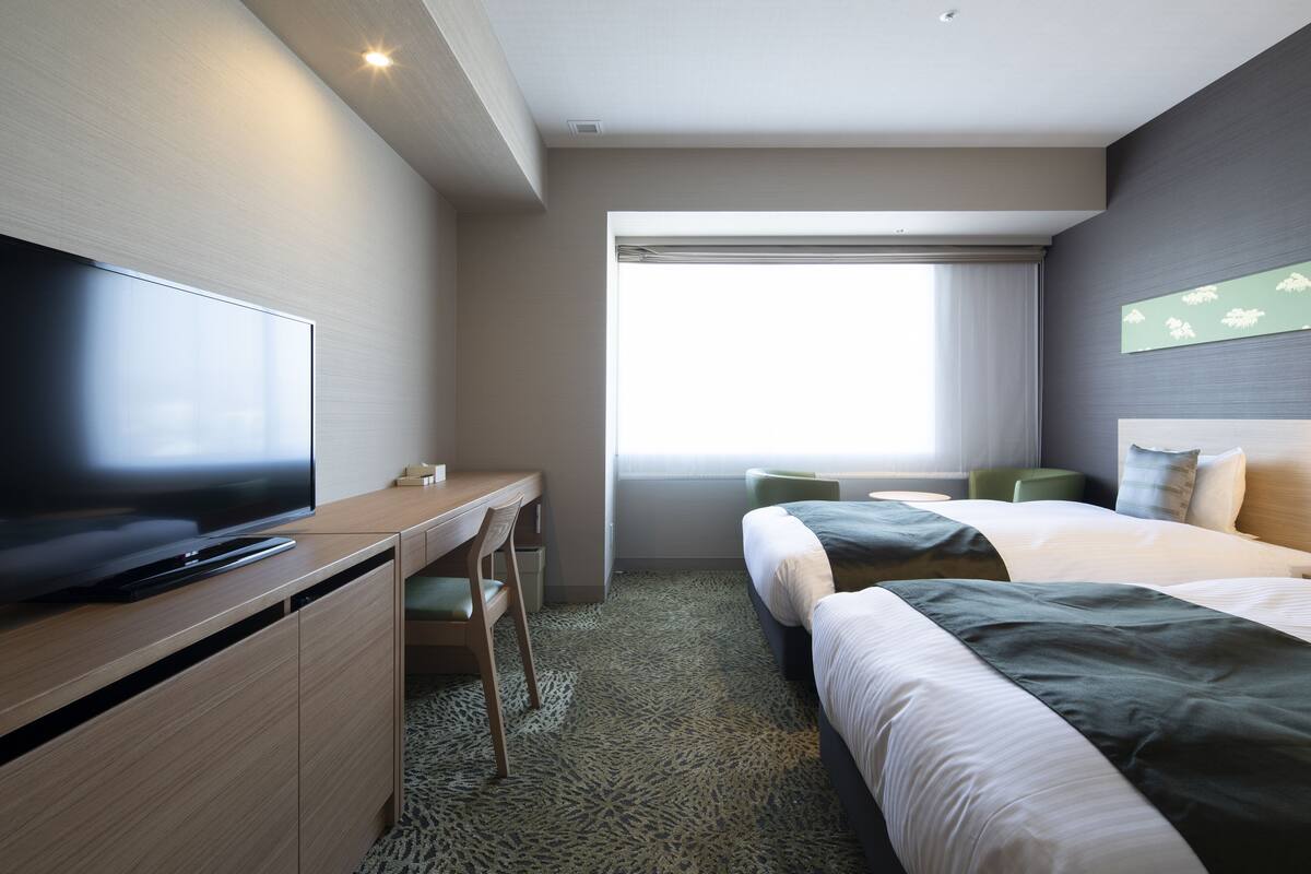 Une chambre d’hôtel moderne dotée d’une télévision à écran plat, d’un bureau, de deux lits et d’une grande fenêtre offrant une vue dégagée.