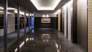 Um corredor moderno com pisos de mármore preto refletivos, portas de vidro e uma obra de arte emoldurada na parede.