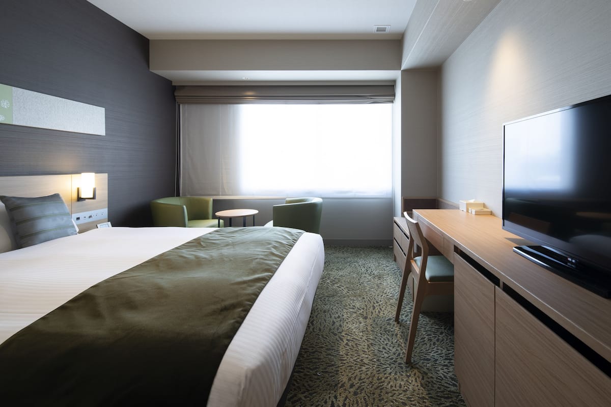 Une chambre d’hôtel avec un lit, un bureau, une télévision et une fenêtre avec des rideaux.