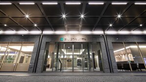 Entrada de um edifício moderno, com portas de vidro, uma placa sobre a entrada e teto com iluminação embutida.