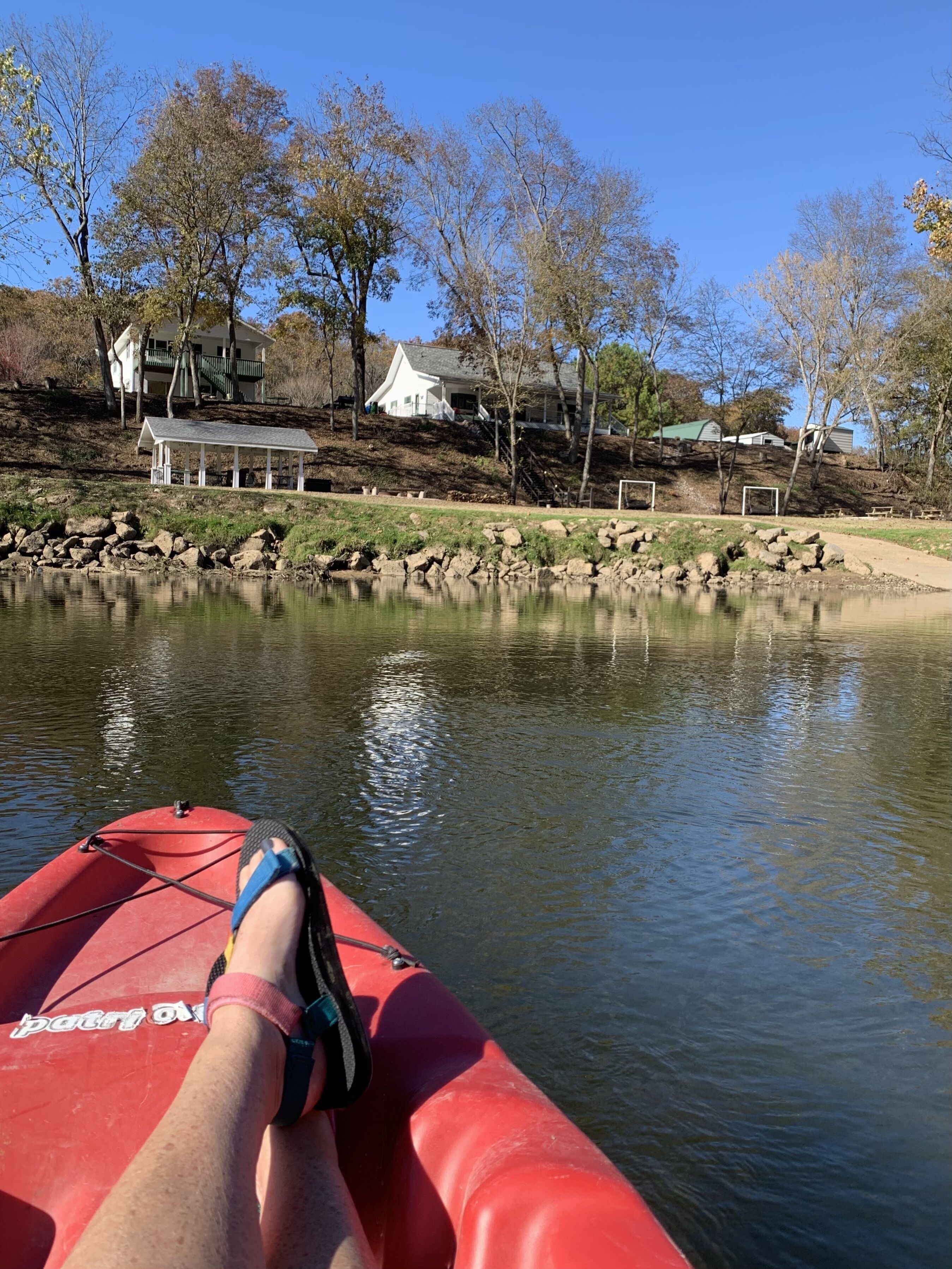 A red kayak on a calm river with a view of a white gazebo and houses in the background.
