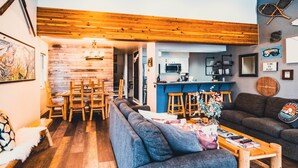 Una sala de estar acogedora con un sofá azul, una mesa de centro de madera y una zona de cocina con barra.