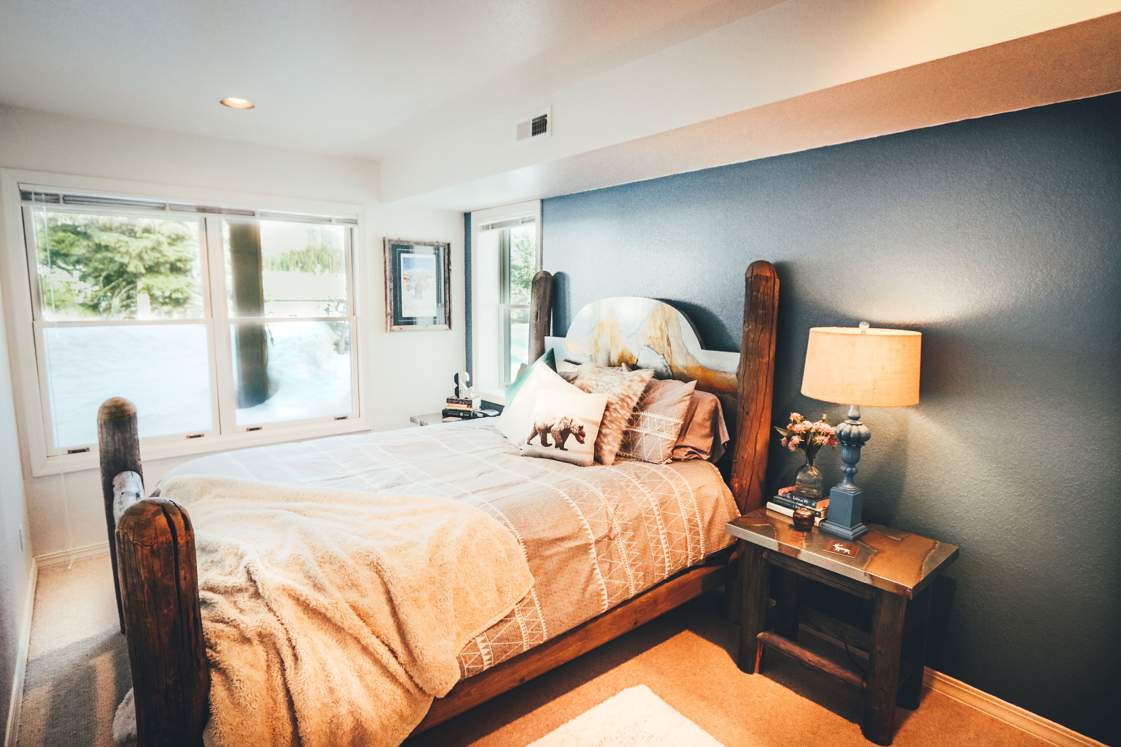 A bedroom with a large bed, a nightstand, a lamp, and a window with blinds.