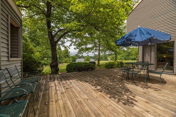 A wooden deck with metal chairs and a table, a blue umbrella, and a view of a lake and trees. - Geneva View by Innsbrook Vacations! (Innsbrook)