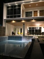 A modern two-story building with a swimming pool, outdoor seating, and a covered patio area.