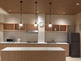 A modern kitchen with wooden cabinets, a central island, a microwave, a kettle, and a refrigerator.