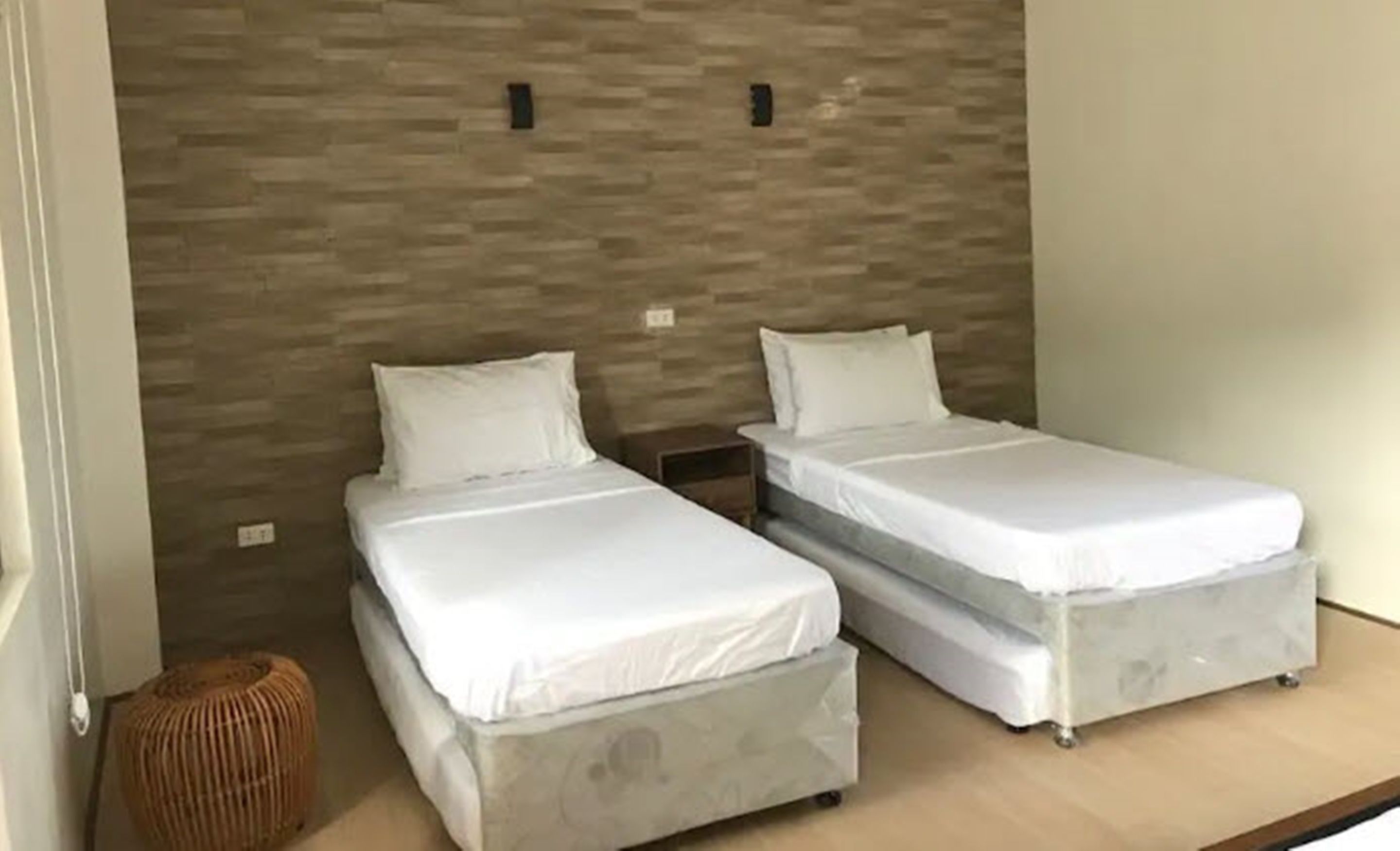 Ein Zimmer mit zwei Einzelbetten, einem kleinen Holzschemel und einer strukturierten Wand.