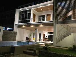 A modern two-story house with a covered outdoor area, a swimming pool, and a staircase leading to the upper floor.