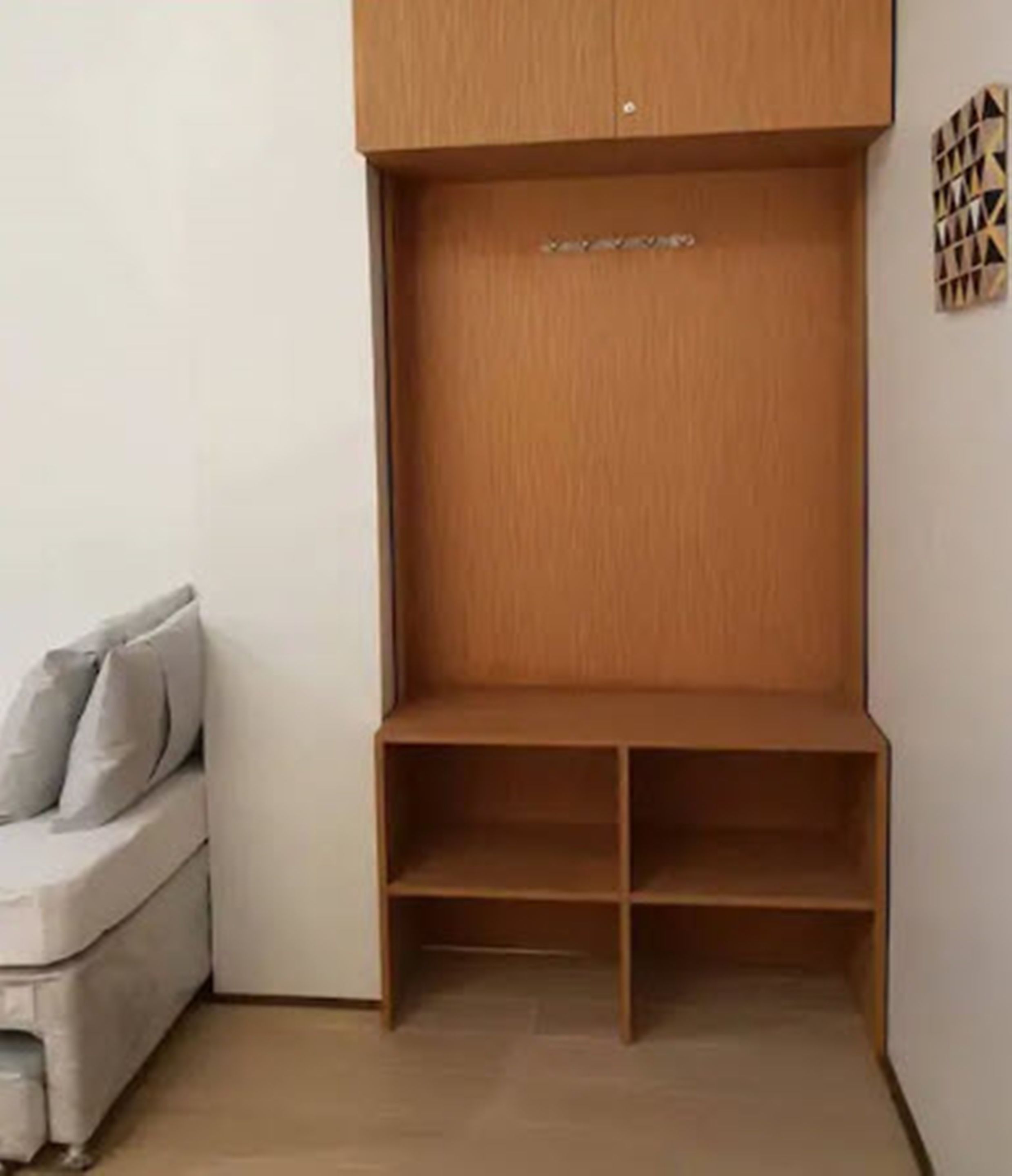 Una habitación con un armario empotrado de madera, un sofá gris y un adorno mural estampado.