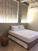 A bedroom with a bed, a woven ottoman, and a wooden slat wall.