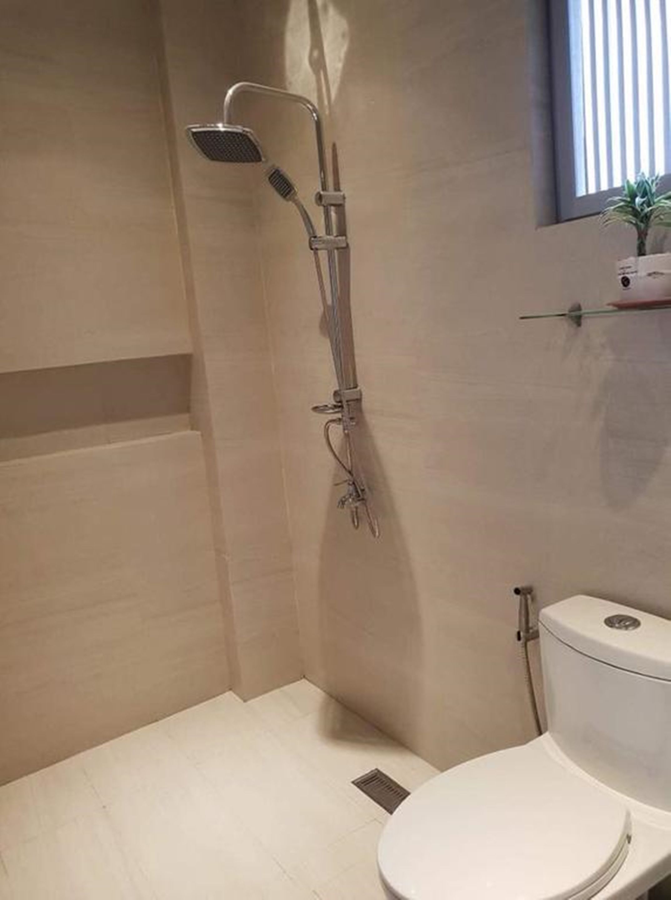 A small bathroom with a shower, toilet, and a window.