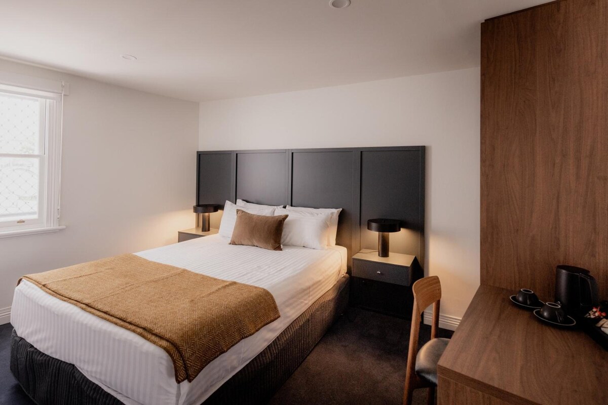 A hotel room with a bed, bedside tables, a desk, and a chair.