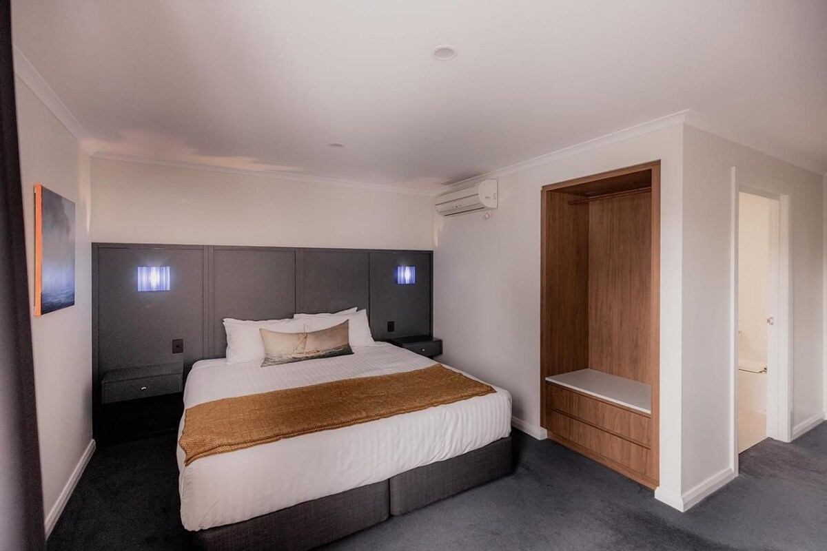 A hotel room with a bed, bedside tables, a wardrobe, and a wall-mounted air conditioning unit.