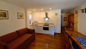 A compact living space with a kitchenette, a sofa, a dining table, and wooden cabinets. - MIRA DOLO 022143-AT-347213 (Madonna di Campiglio)
