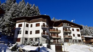 A multi-story hotel with balconies, snow-covered trees, and a clear blue sky. - MIRA DOLO 022143-AT-347213 (Madonna di Campiglio)