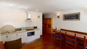 A compact kitchen with white cabinets, a sink, and a stove. There is a dining area with wooden chairs and a table. - MIRA DOLO 022143-AT-347213 (Madonna di Campiglio)