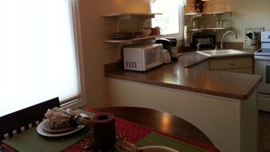A kitchen with a microwave, toaster, sink, and a dining area with a table set for two. - Charming and Convenient! No cleaning fee. Sleeps 6. (Anaconda)
