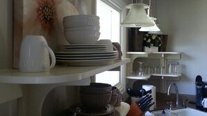A kitchen with white cabinets, a sink, and a countertop with various dishes and utensils. - Charming and Convenient! No cleaning fee. Sleeps 6. (Anaconda)