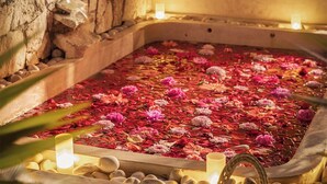Un baño de spa lleno de agua y pétalos de rosa, rodeado de velas y plantas en macetas.