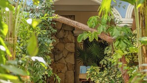 Un muro de piedra con un banco, rodeado de abundante follaje y plantas en macetas.