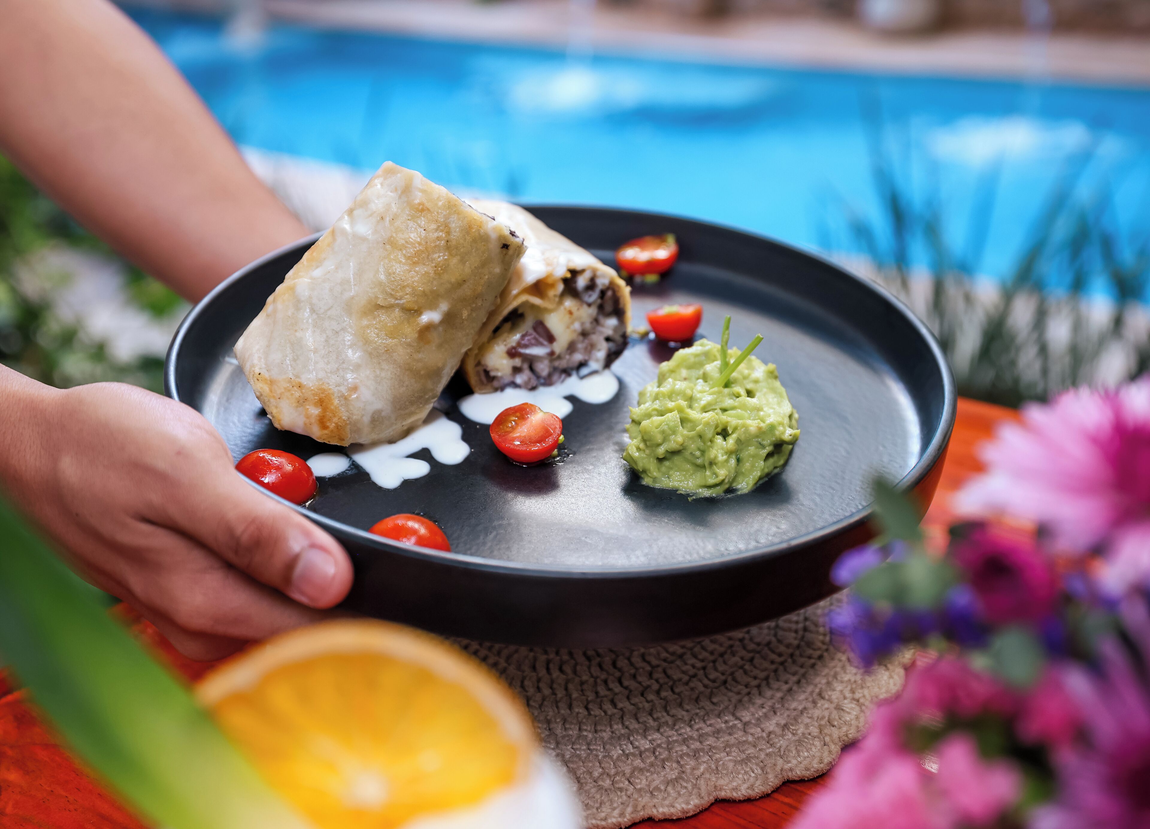 A plate with a sandwich, guacamole, and cherry tomatoes.