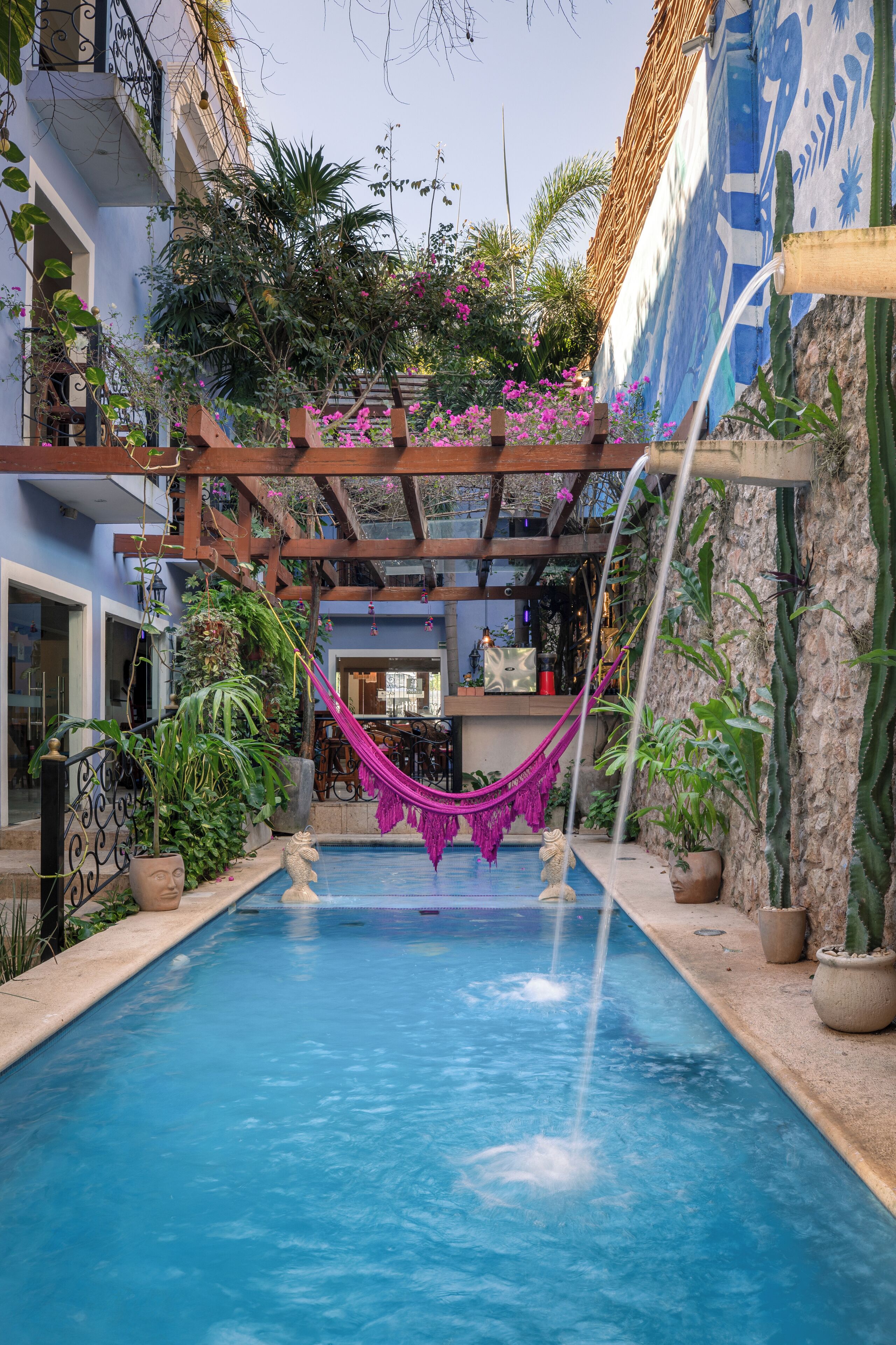 A pool area with a hammock, potted plants, and a mural on the wall.