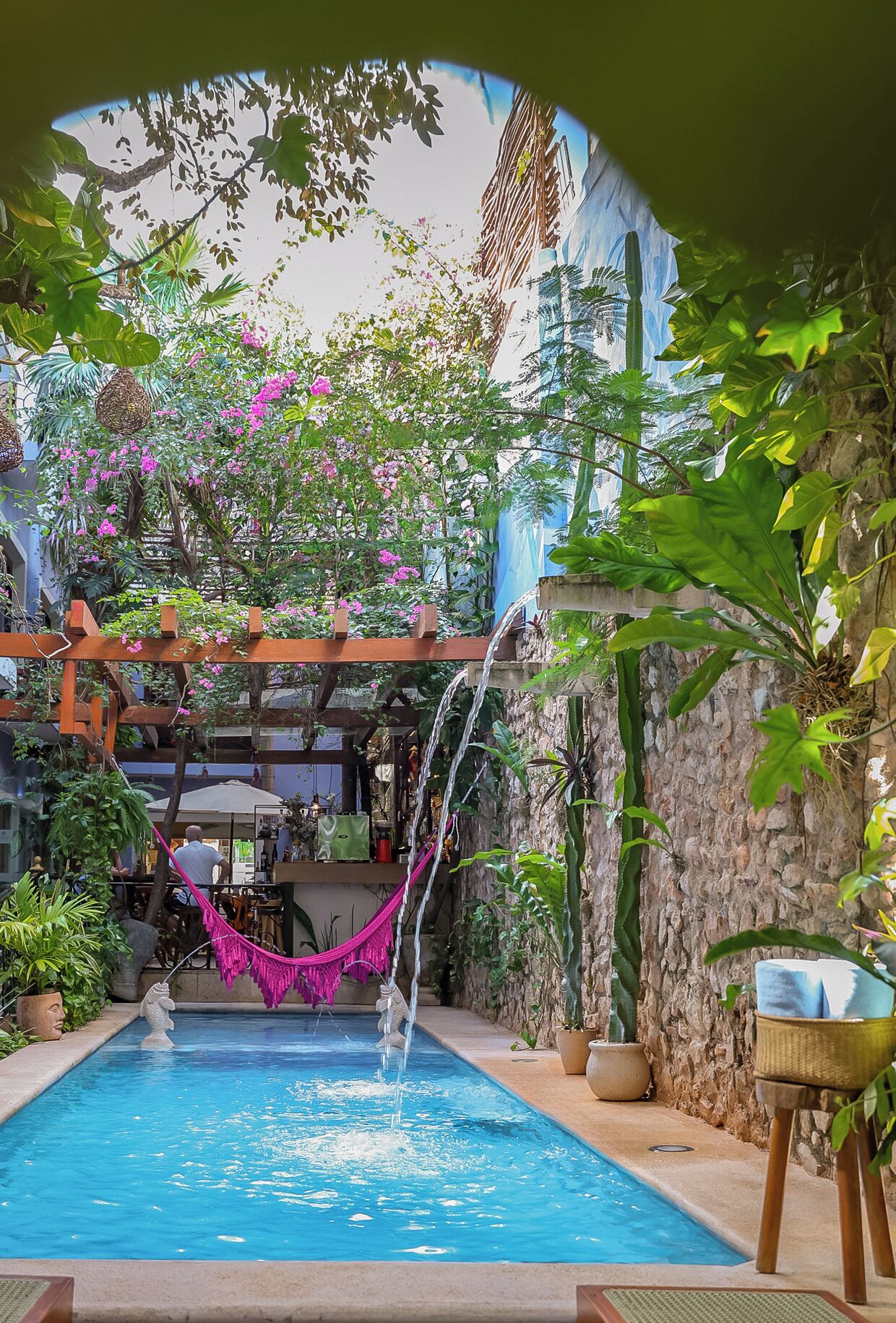 A pool with a waterfall feature, surrounded by lush greenery and a hammock.