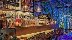 Zona de bar con mostrador de madera, taburetes y una variedad de botellas y vasos.