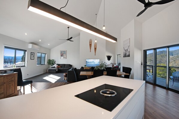 Une cuisine moderne dotée d’un îlot central, d’un coin repas avec une table et des chaises, et d’une grande fenêtre offrant une vue sur l’extérieur.