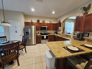 A modern kitchen with stainless steel appliances, granite countertops, wooden cabinets, and a dining area with a table and chairs.