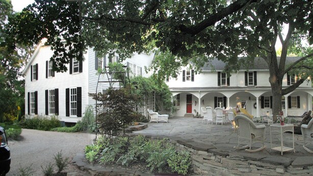 A traditional white building with black shutters, a stone patio, and outdoor seating.