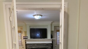 An open doorway leading to a bedroom with a television, a fireplace, and a bed with a white comforter.