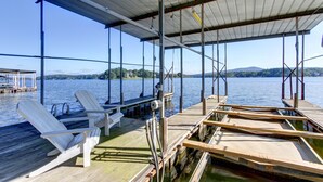 Un muelle cubierto con sillas y un banco de madera, con vistas a un lago tranquilo y colinas al fondo.