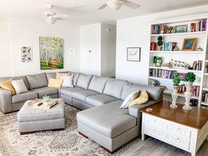 A modern living room with a grey sectional sofa, a white sideboard, and a bookshelf filled with books and decorative items.