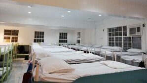 A hospital ward with multiple beds arranged in rows, each with white linens and pillows.