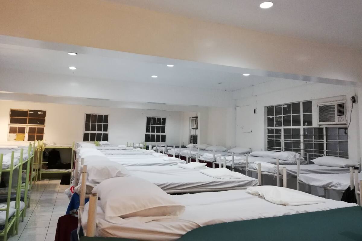 A hospital ward with multiple beds arranged in rows, each with white linens and pillows.
