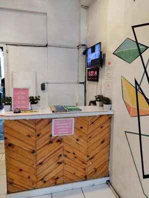 A reception desk with a digital clock, a sign indicating the branch, and a wall with geometric art. - Dormitels.ph Ermita (Manila)