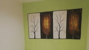 A single-bed room with a green accent wall, a large painting of trees, and a tiled floor.