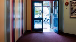 A hallway with a red carpet leading to a glass door entrance.