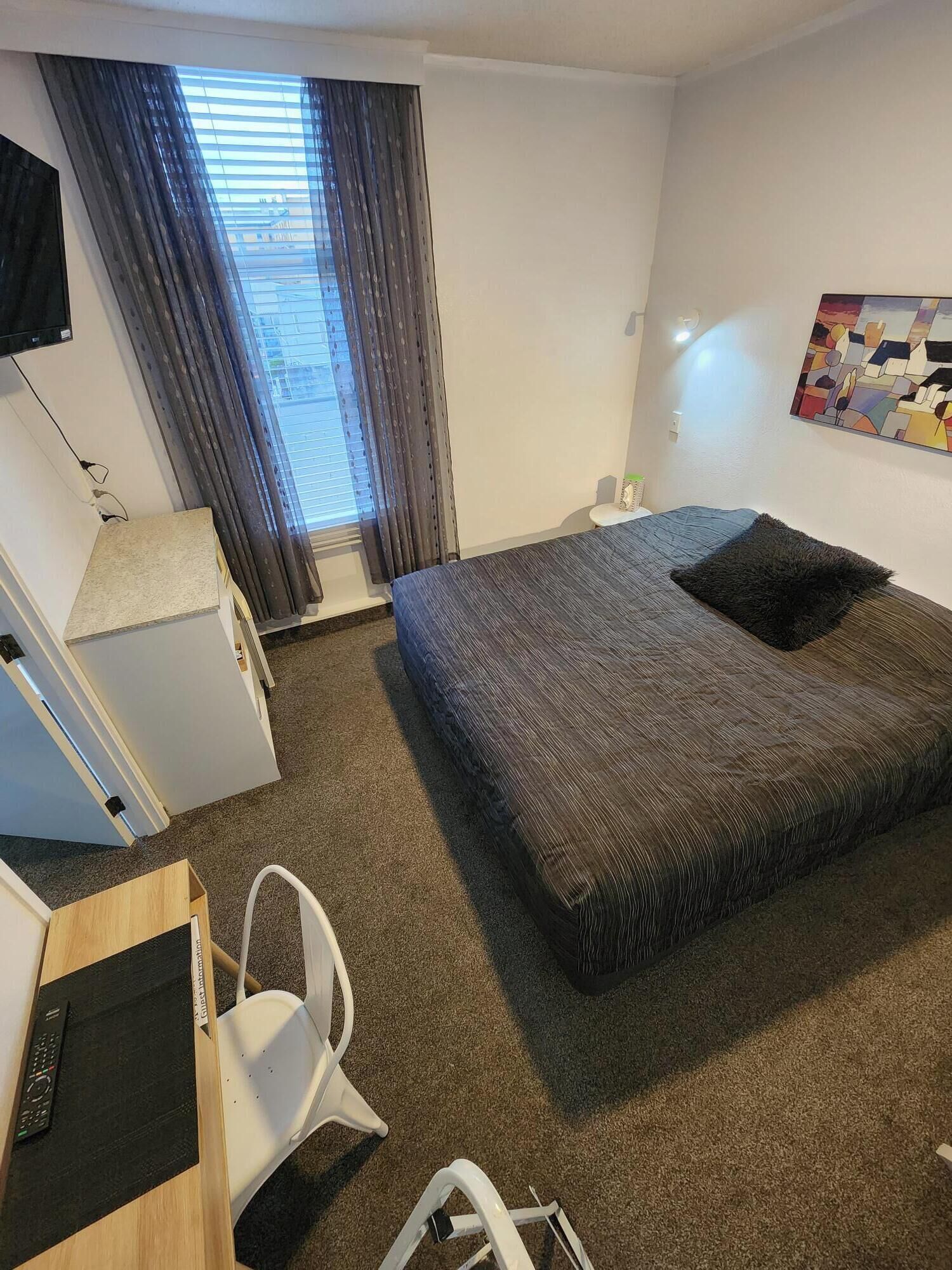 Habitación de hotel con cama, escritorio, silla, televisor y ventana con cortinas.